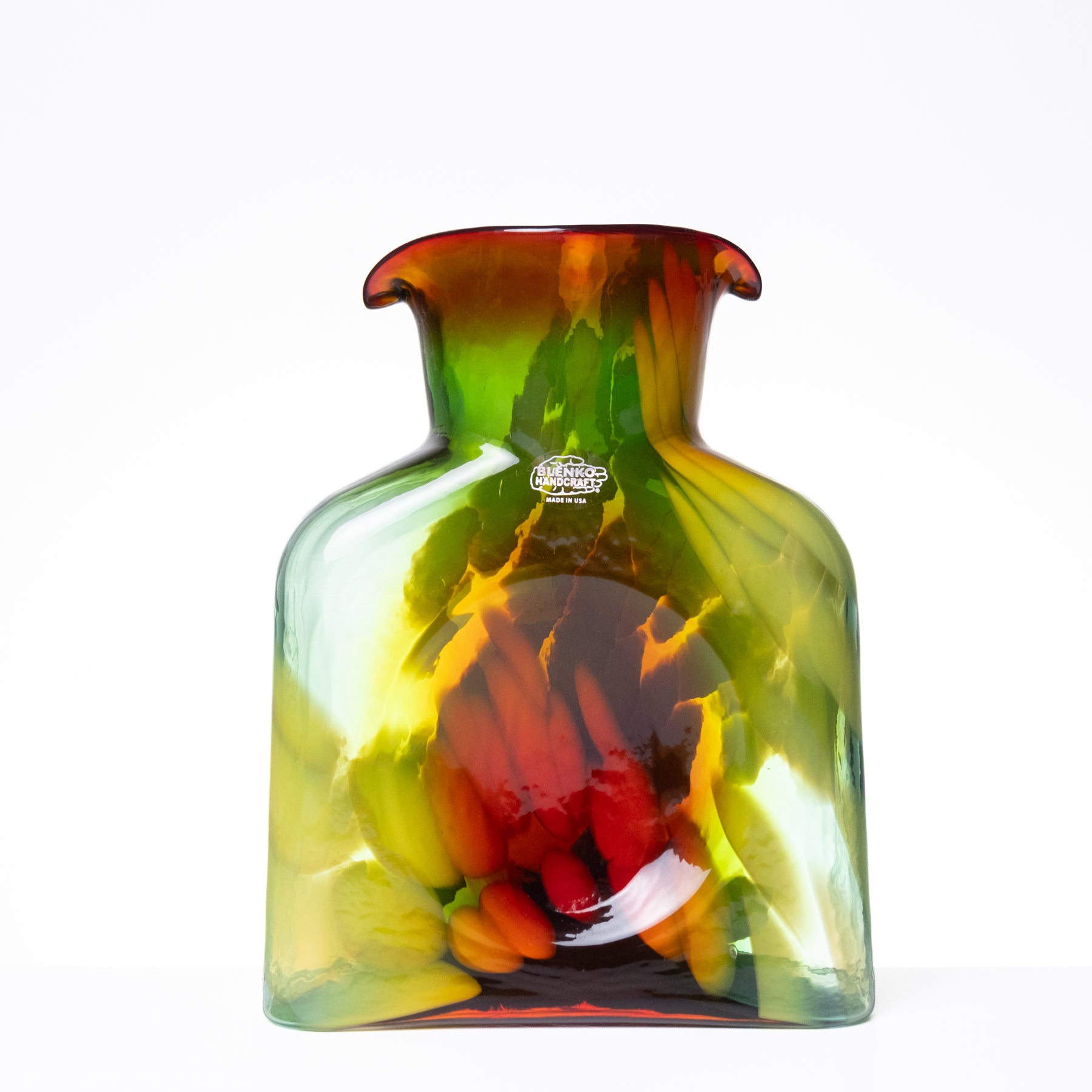 A hand-blown glass vase with a rounded body and flared rim, featuring a marbled color palette of green, yellow, orange, and red on a white background.