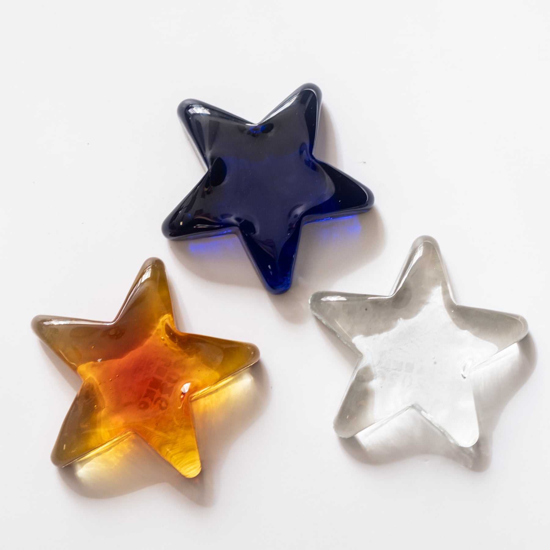 Three star-shaped objects in blue, orange, and clear on a white background