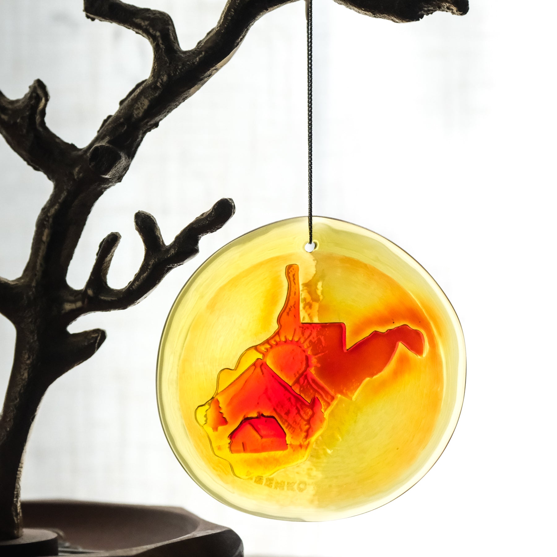 Decorative hanging disc with WV shaped stamp against a yellow background, attached to a branch.