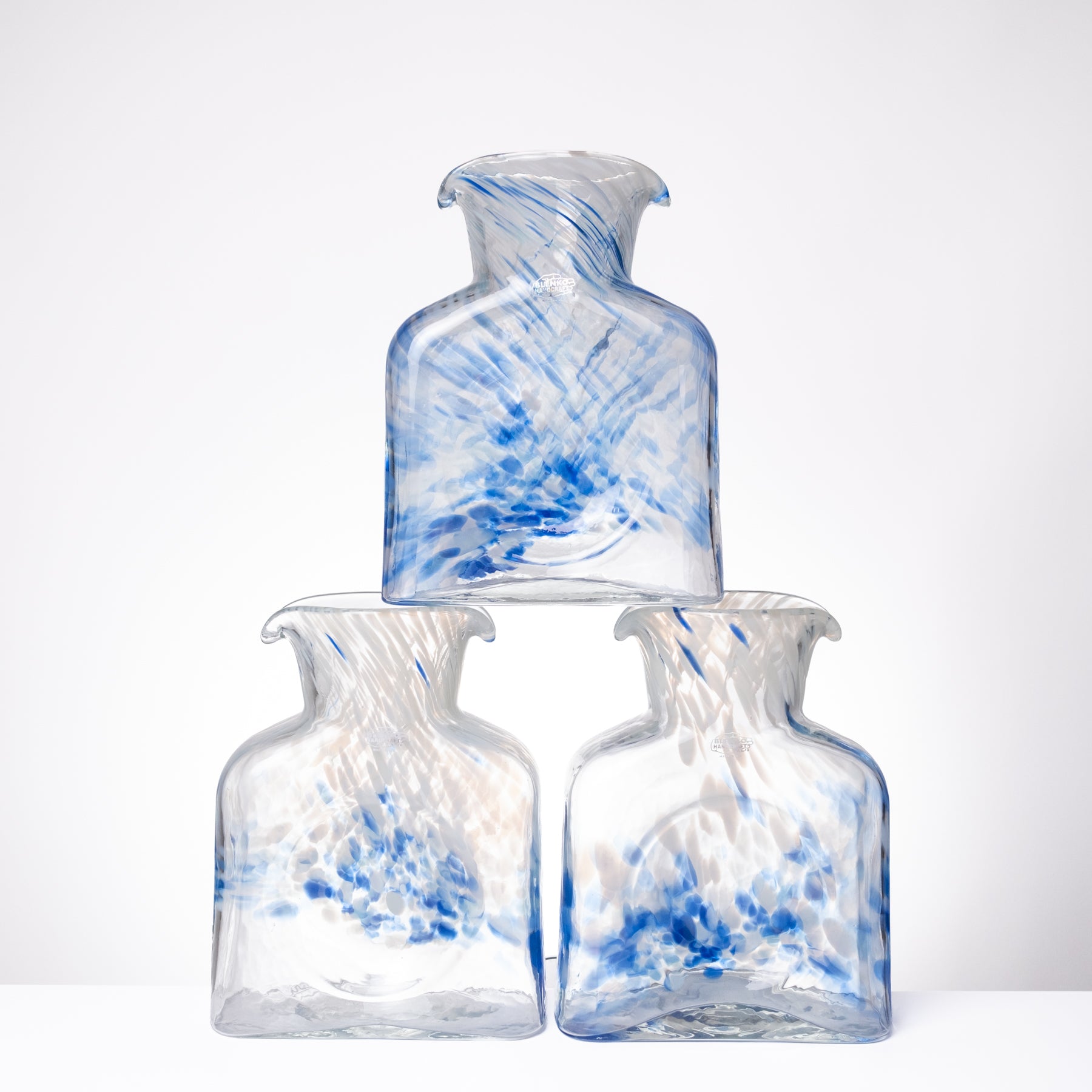Three clear glass bottles with blue marbled swirls, arranged in a pyramid stack on a white surface against a white background.