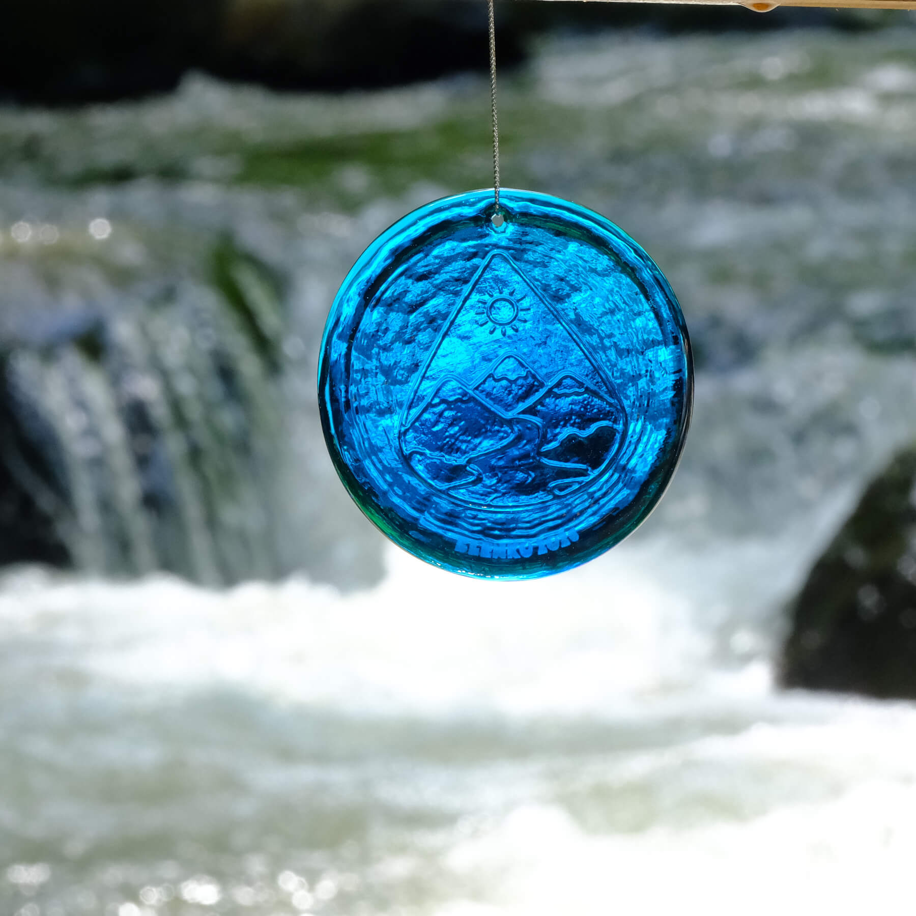 Blue glass ornament with a geometric design hanging against a blurred natural background