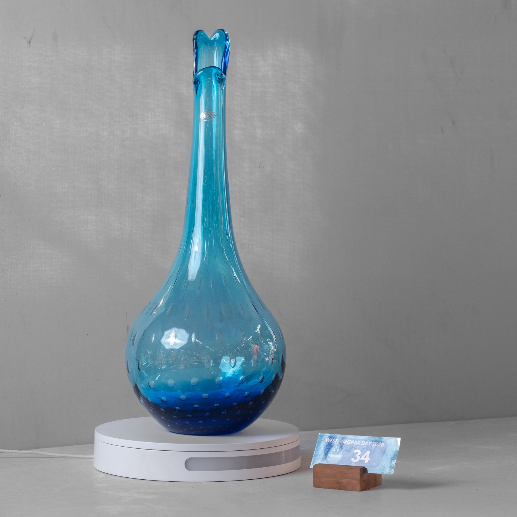 A translucent blue glass decanter with a flared stopper, resting on a white circular charging base against a gray wall.