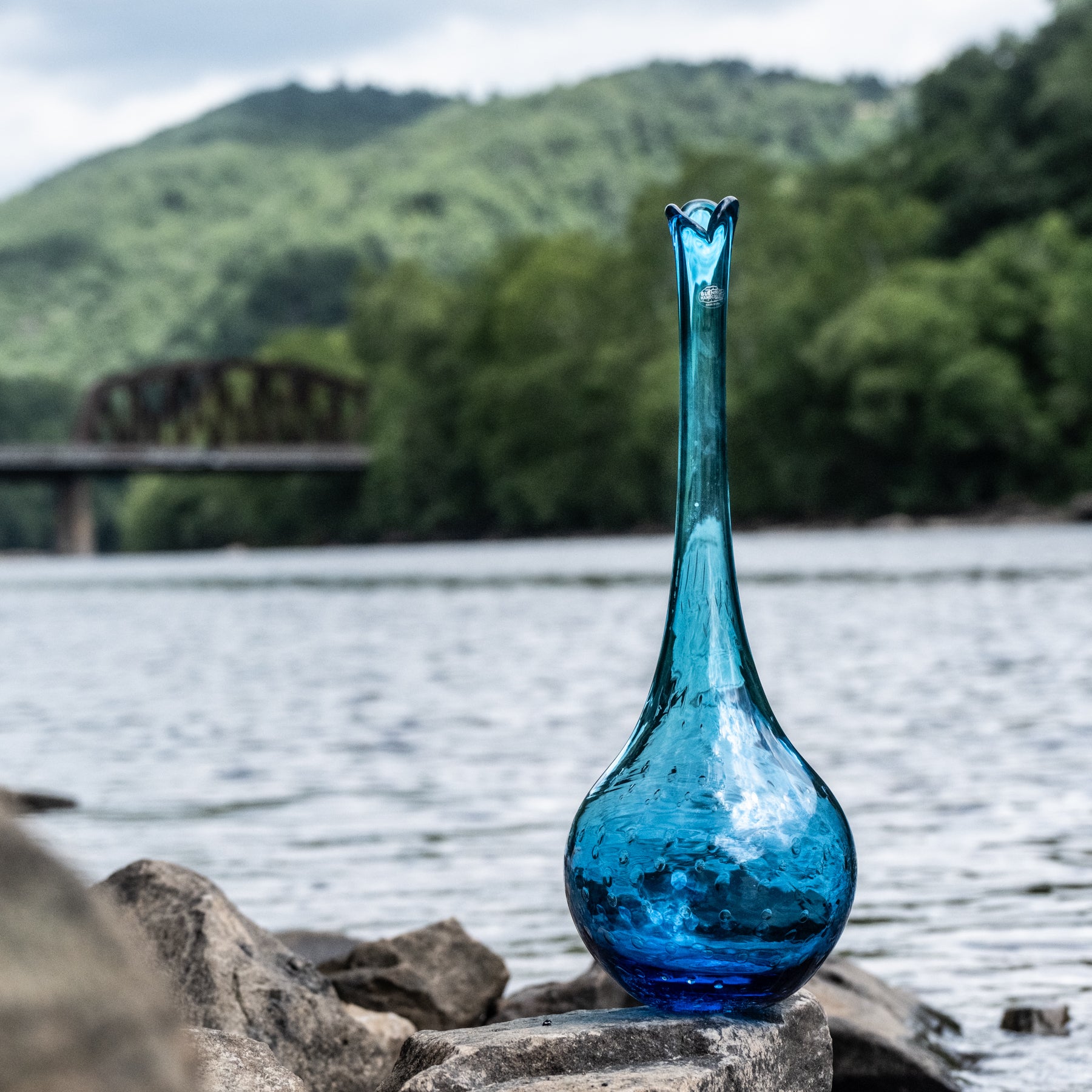 Blue glass vase on rocks by a lake with a blurred natural background