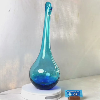 A translucent blue glass vase with a flared neck and dotted pattern, displayed on a white circular base against a light gray wall.