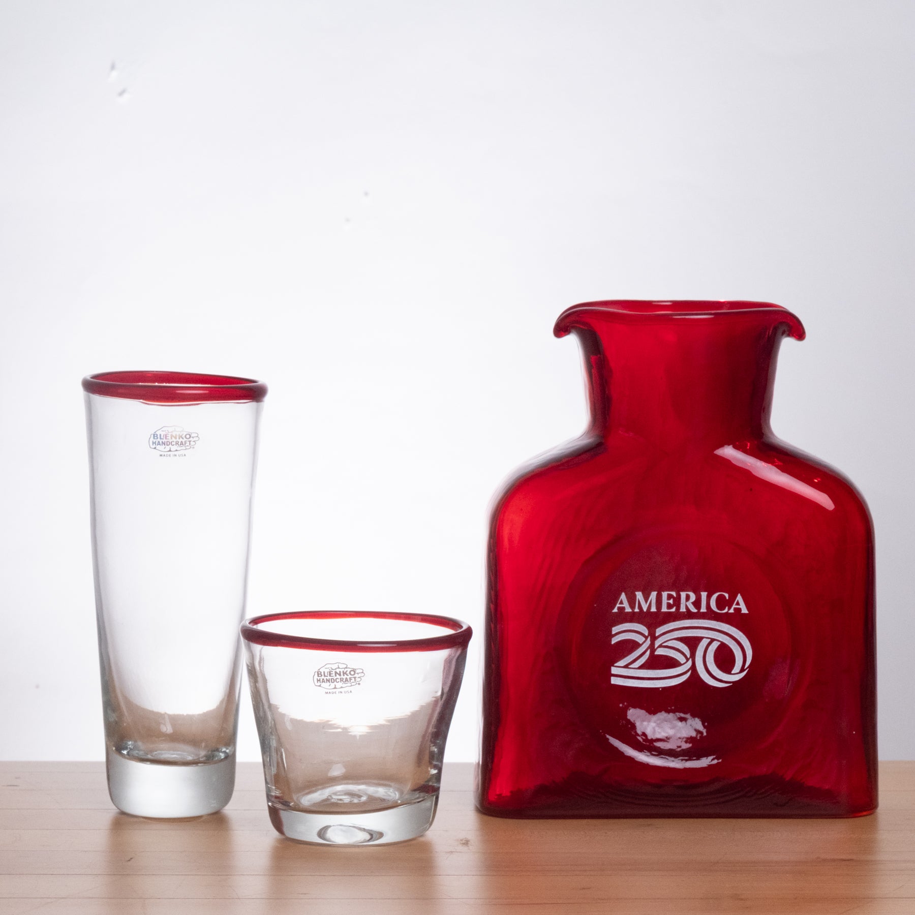 Red bottle and glasses with 'America 250' branding on a white background