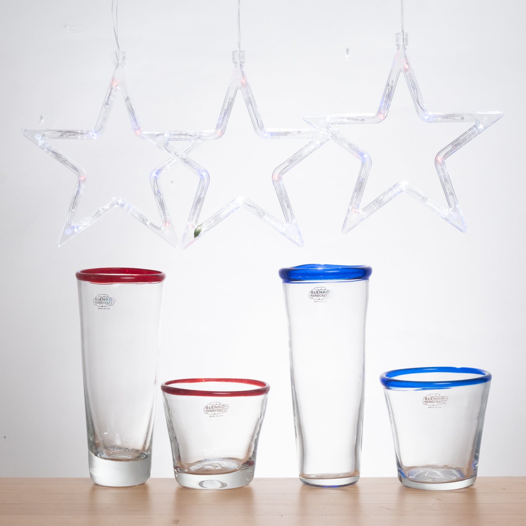 Set of four glass tumblers with colored rims on a wooden surface.
