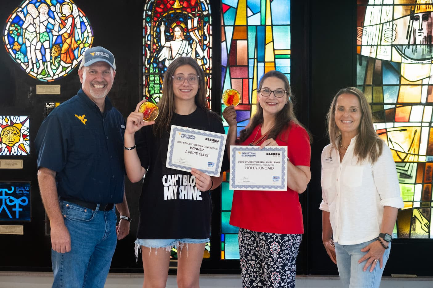 Four people holding certificates in front of a stained glass window